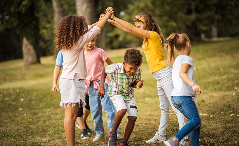 Group of children outdoors forming a human tunnel with raised arms as another child runs through