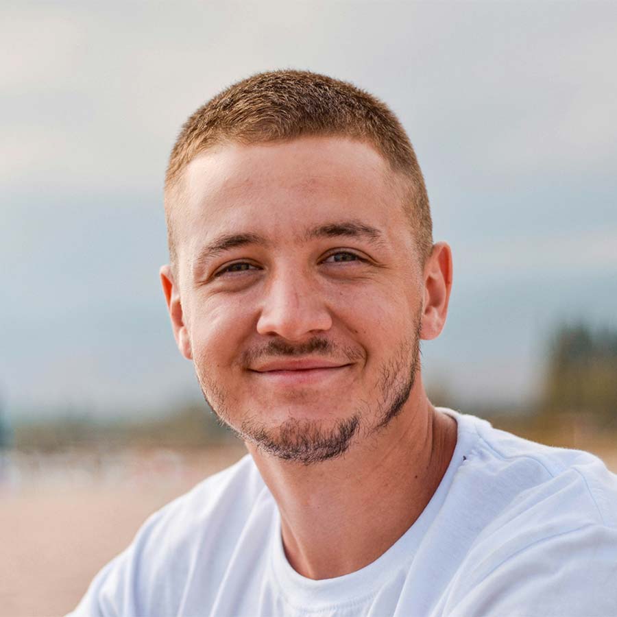 Smiling young man with short hair and light stubble wearing a white T-shirt on a beach background