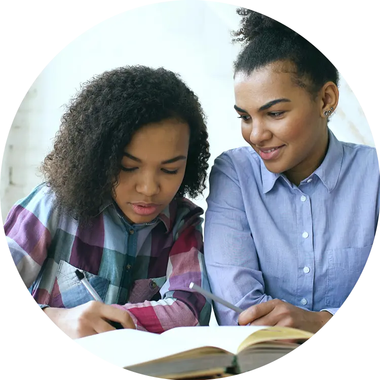 Young woman helping a girl with homework, both writing beside an open textbook