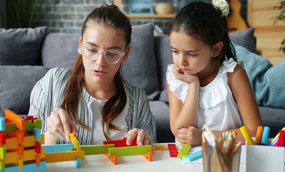 Adult guiding girl assembling colourful interlocking construction blocks on a table
