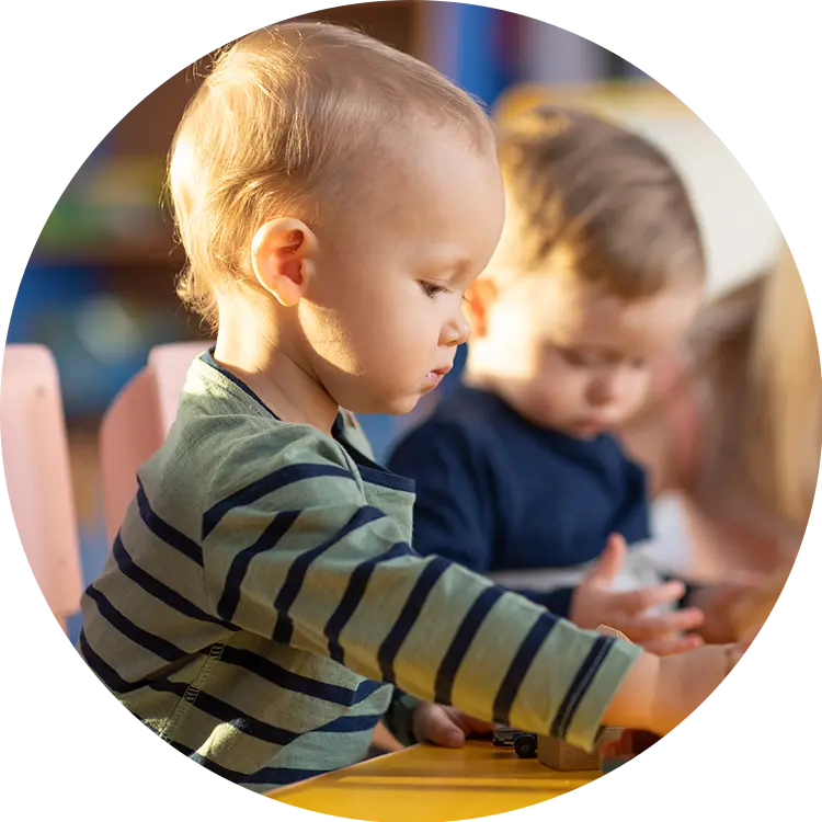 Toddler in a striped top and another child playing with toy cars at a daycare table
