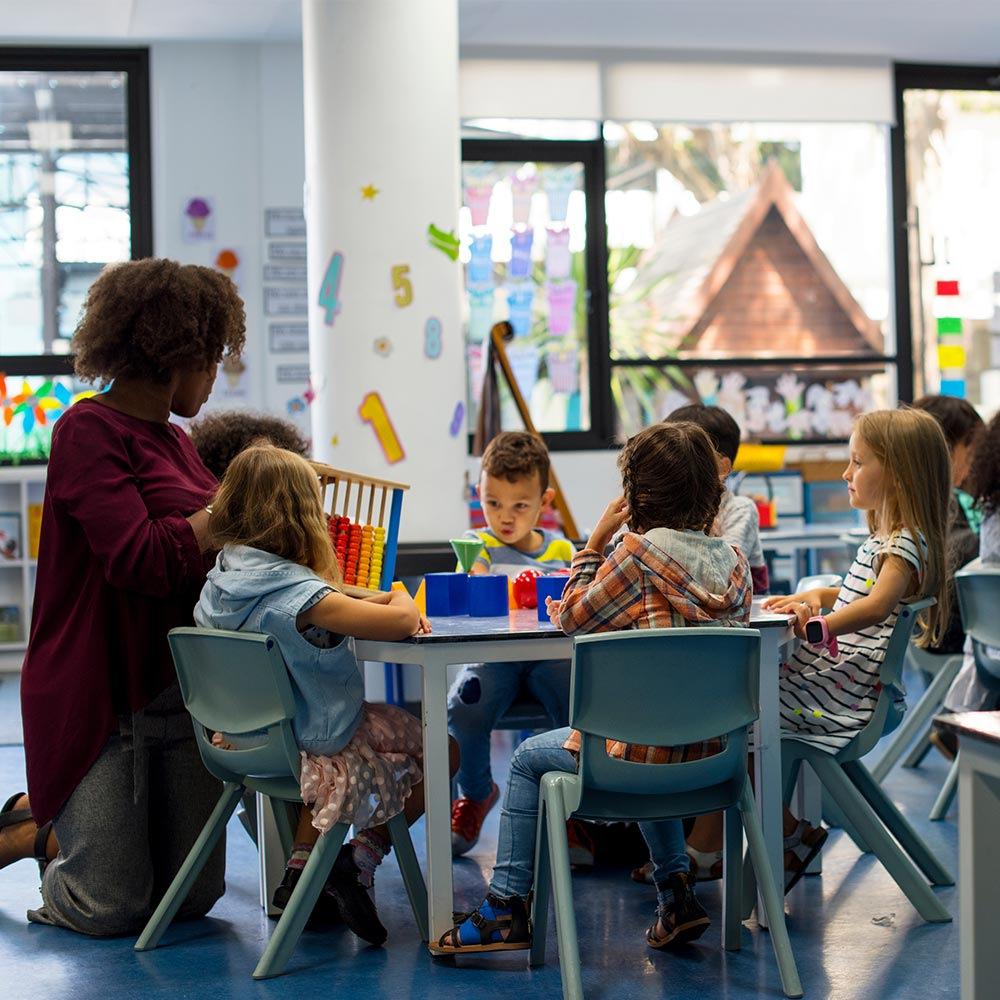 Early years teacher kneeling with preschool children at a table using an abacus and colourful learning toys