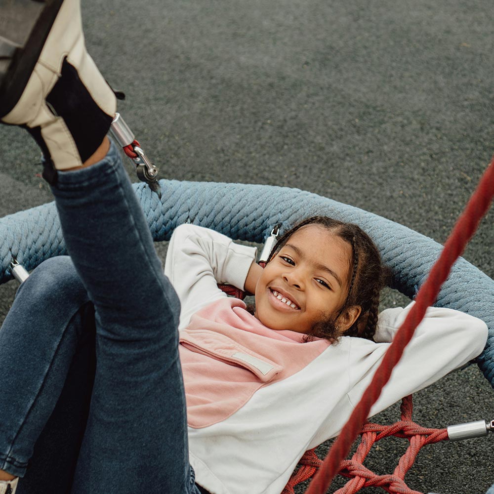 Child smiling and reclining in a circular net rope swing at a playground