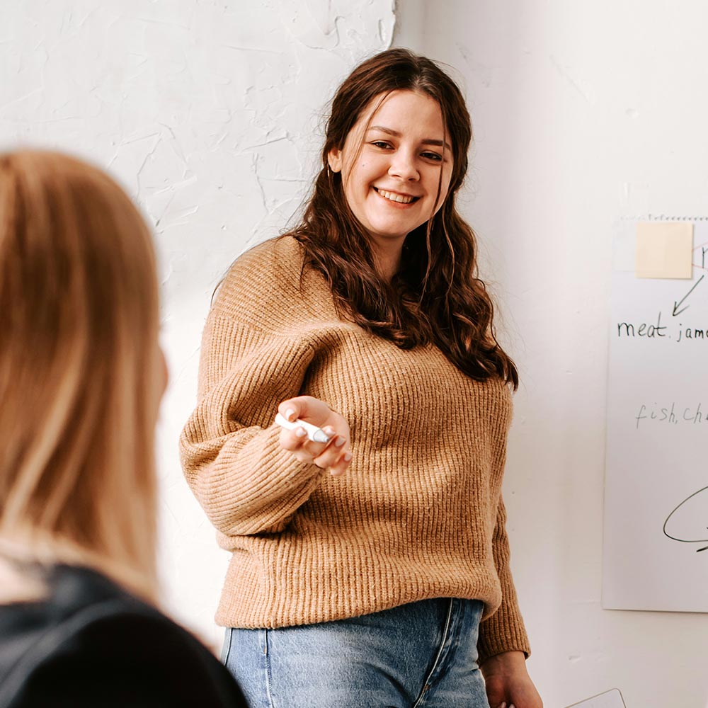 Smiling woman holding a marker and presenting at a whiteboard to a colleague